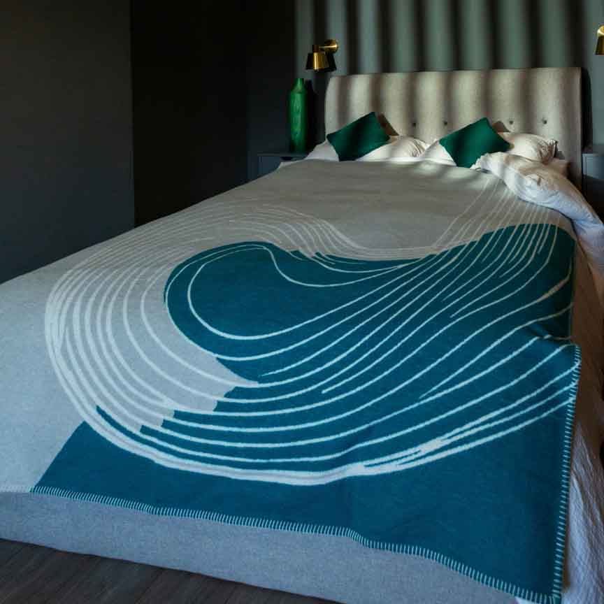 Teal and white patterned blanket draped over a bed in a bedroom setting.