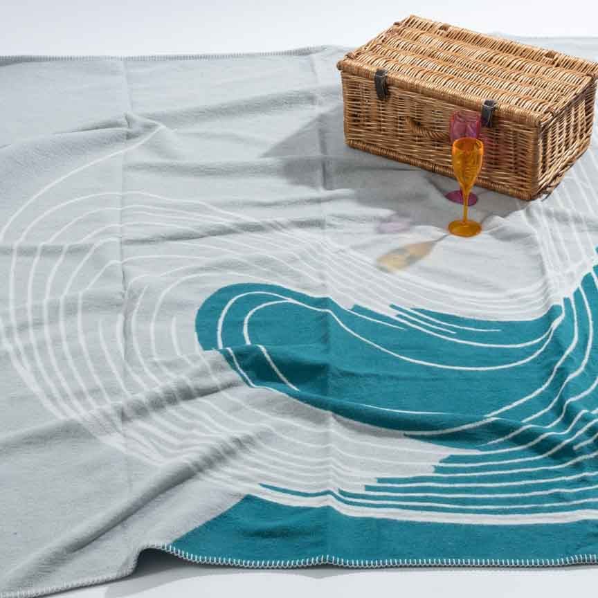 Blanket with wave pattern on a flat surface, featuring a picnic basket and glass.