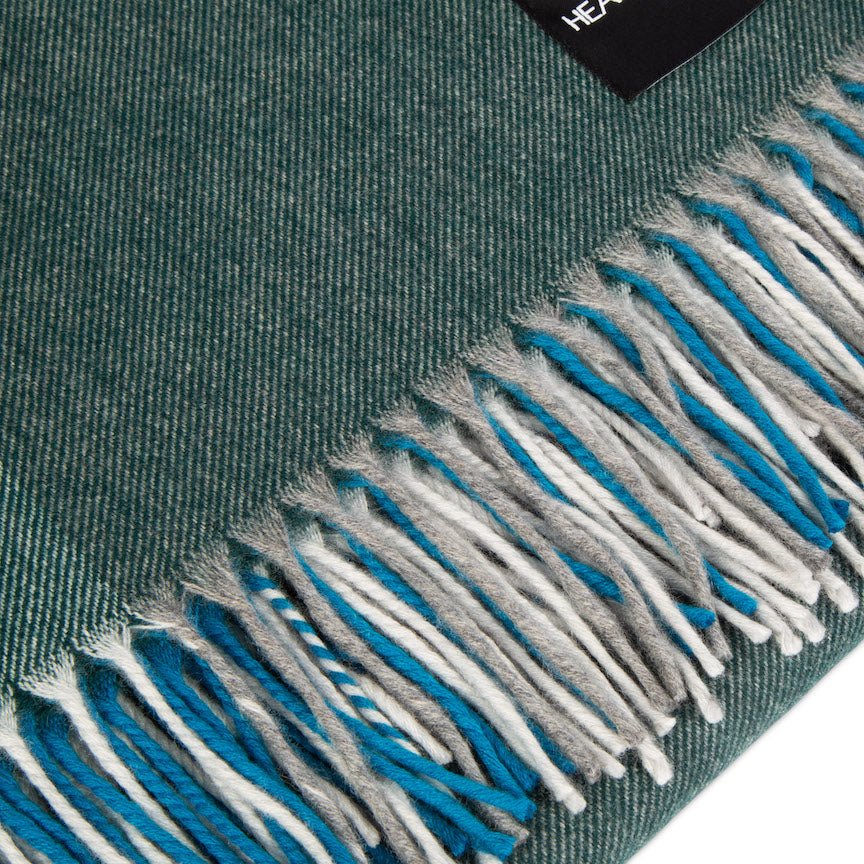 Close-up of a green scarf with blue and white fringe on a white background