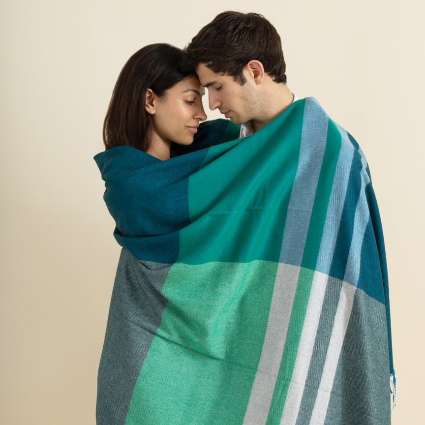Two people wrapped in a green and blue striped blanket against a beige background