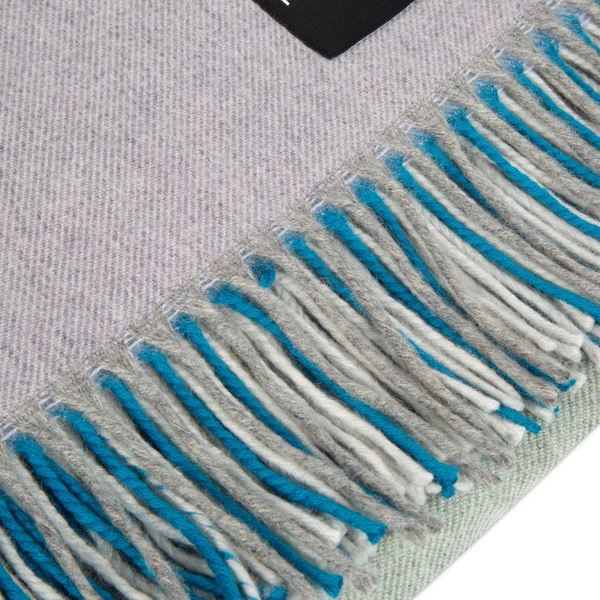 Close-up of a grey fabric with blue and white fringes on a textured surface.
