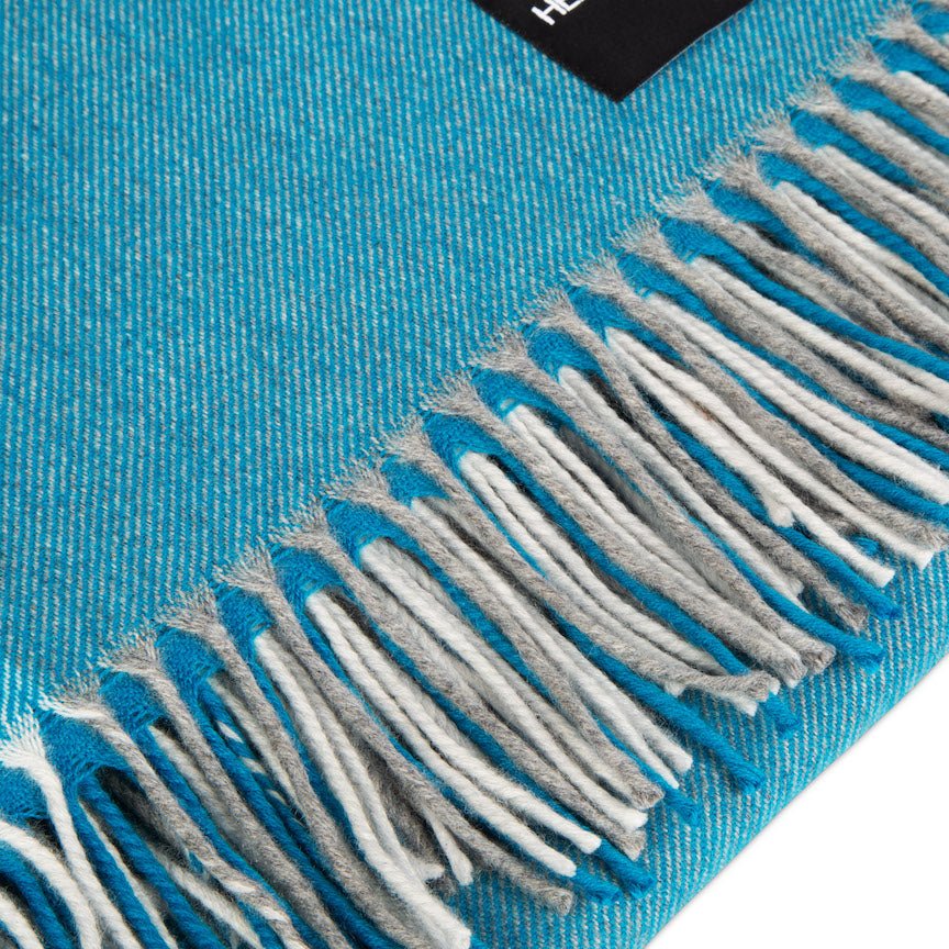 Close-up of a blue blanket with white and gray fringes on a white background