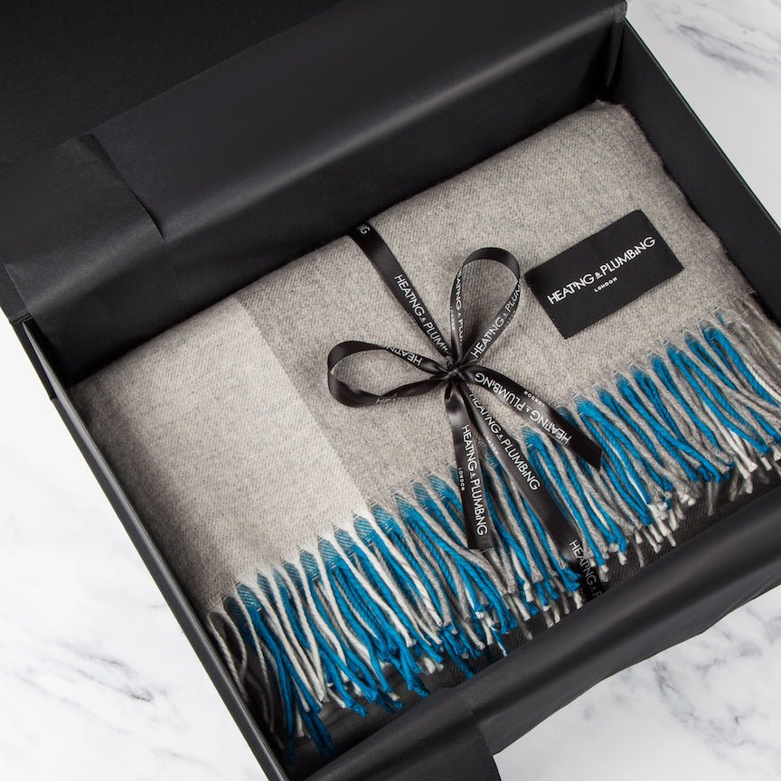 Grey blanket with blue fringe and black ribbon in a black box, branded 'Heating & Plumbing'.