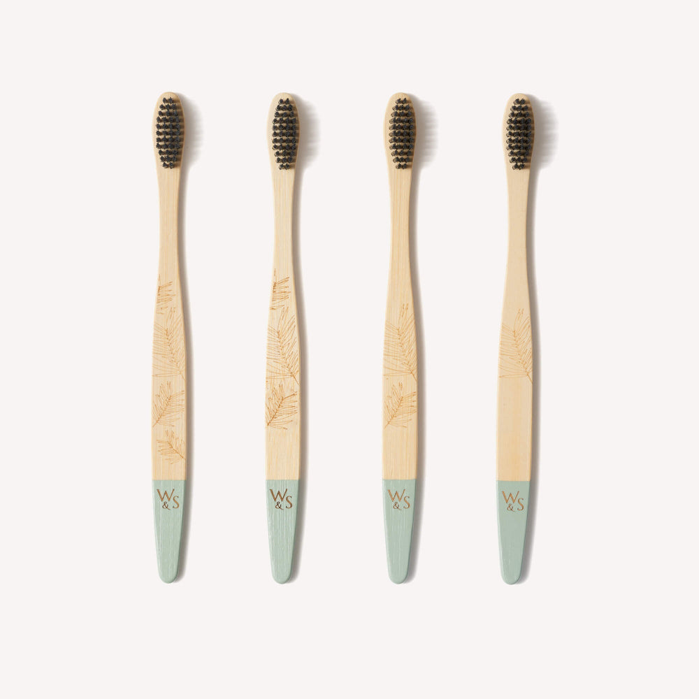 Four bamboo toothbrushes with green handles on a white background