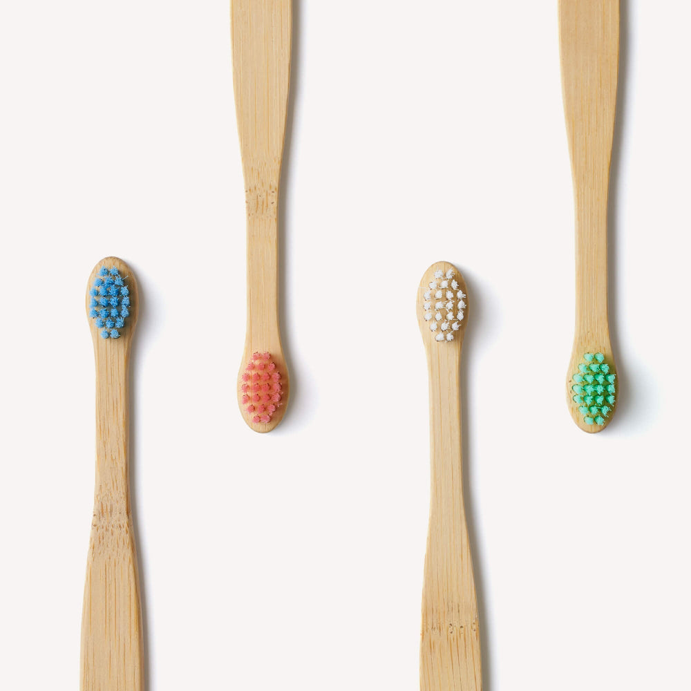 Set of four bamboo toothbrushes with coloured bristle heads on a white background