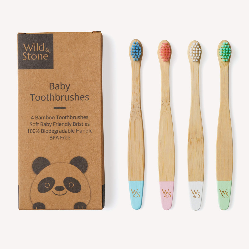 Set of four bamboo baby toothbrushes with coloured bristles and packaging by Wild & Stone on a white background.