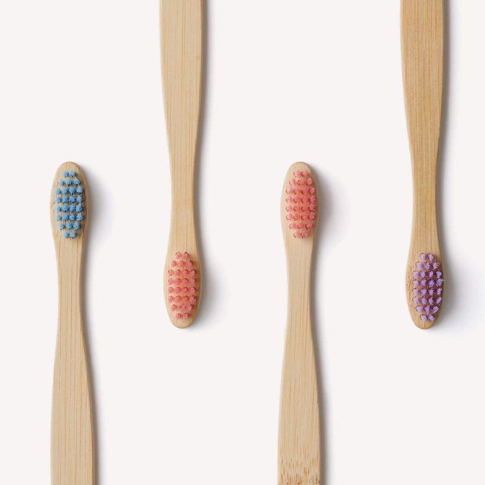 Four bamboo toothbrushes with coloured bristles on a white background