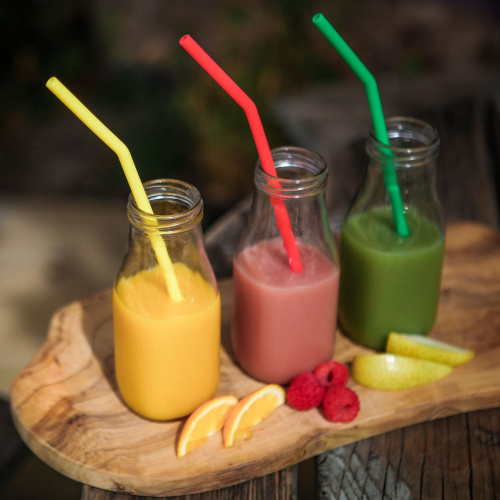 Three glass bottles with colourful straws and fruit on a wooden surface
