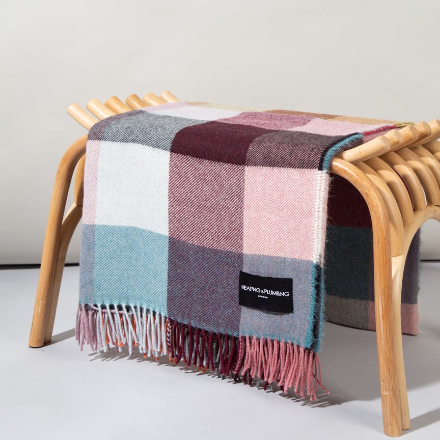 Plaid blanket with fringes draped over a wooden stool on a light grey background