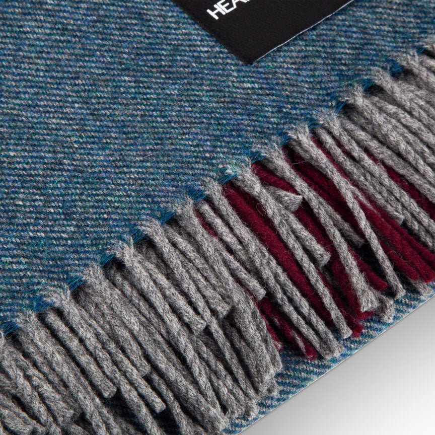 Close-up of a blue and gray plaid blanket with fringes, featuring a brand label.