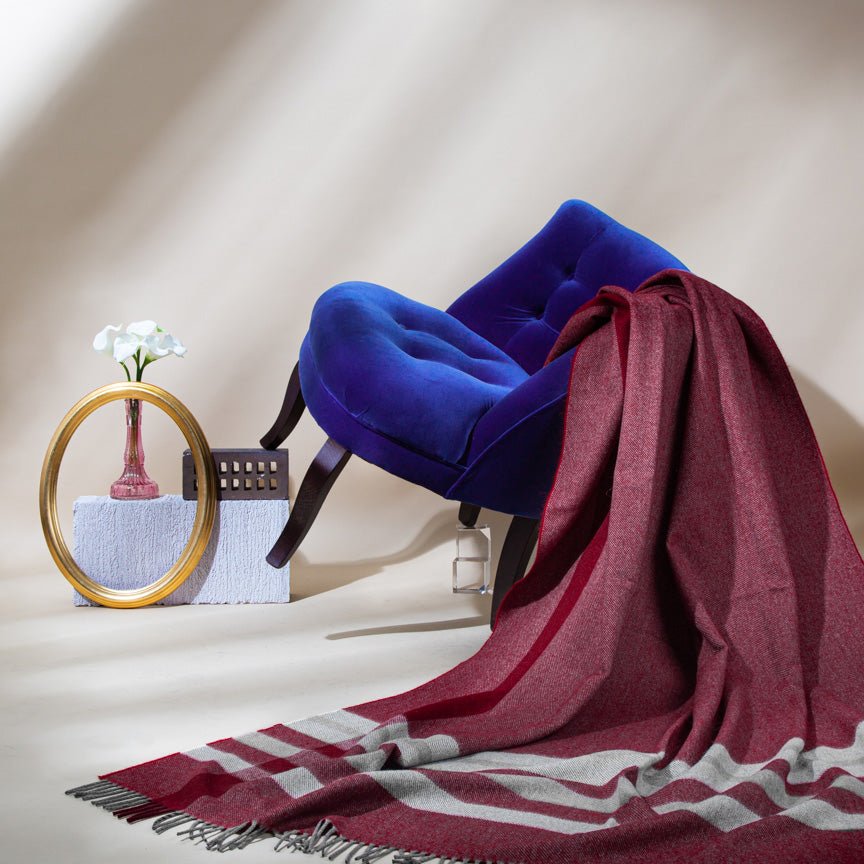 Blue chair with a red and grey striped alpaca and lambswool blanket draped over it, next to a mirror and small table.