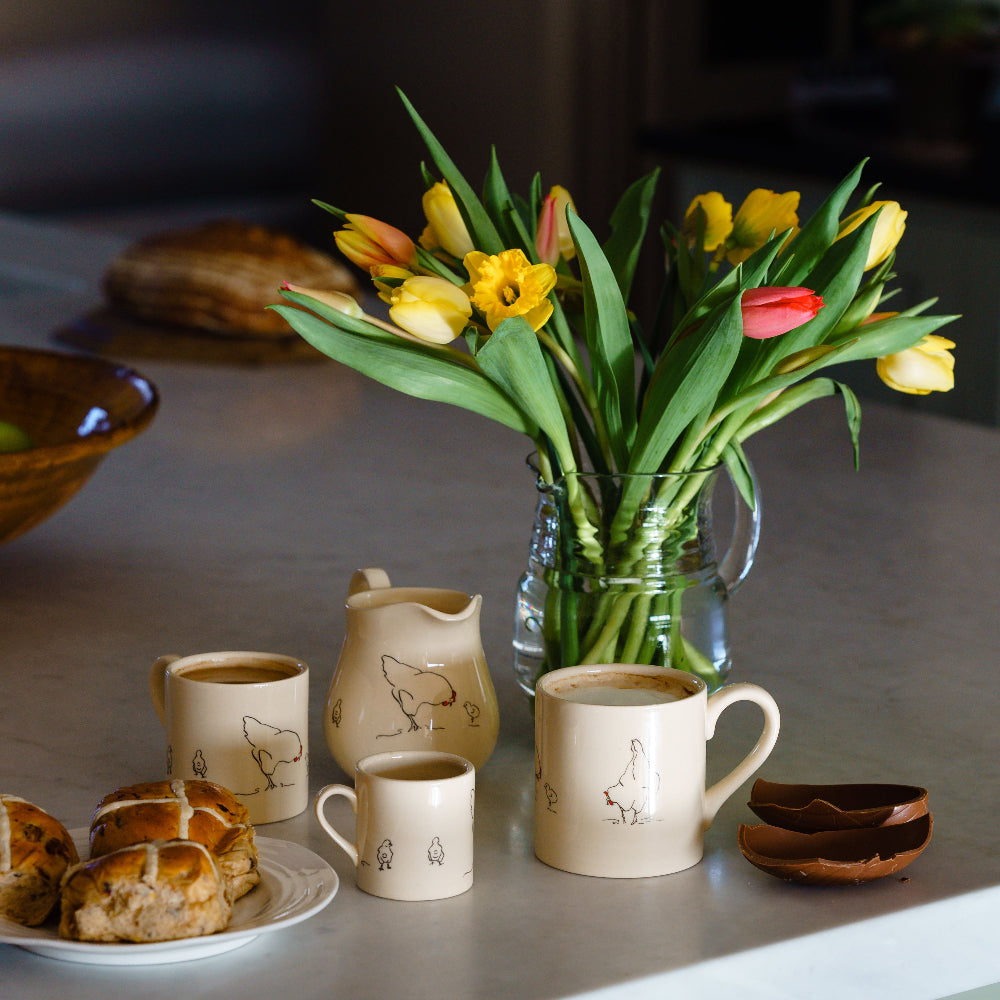 Ceramic Chicken Mugs and Jugs Easter Egg and Hot cross Buns on a kitchen worktop with tulips in a jar