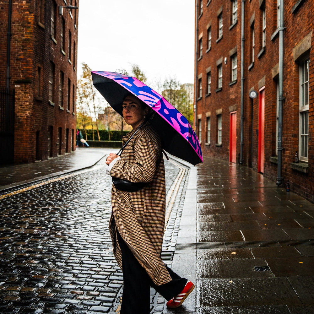Person holding a colourful umbrella on a rainy street with brick buildings.