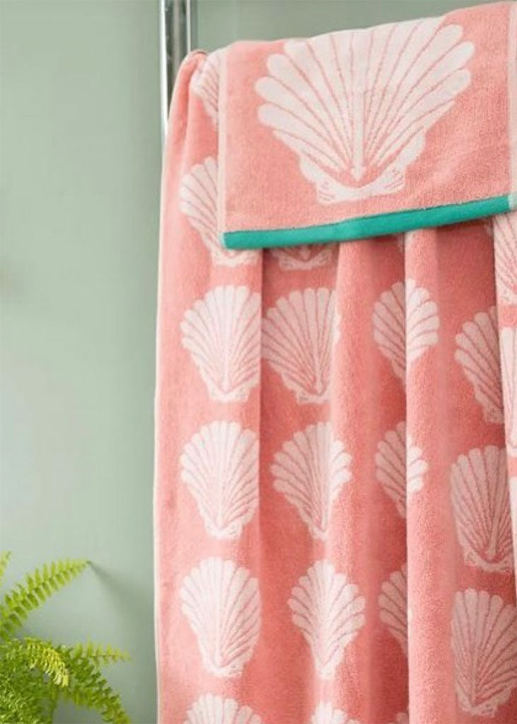 Pink towel with white shell pattern draped over a green object against a light green background