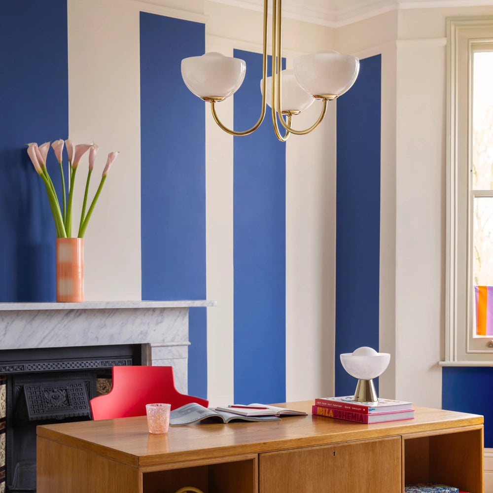 Modern living room with blue striped wall, wooden desk, and red chair.