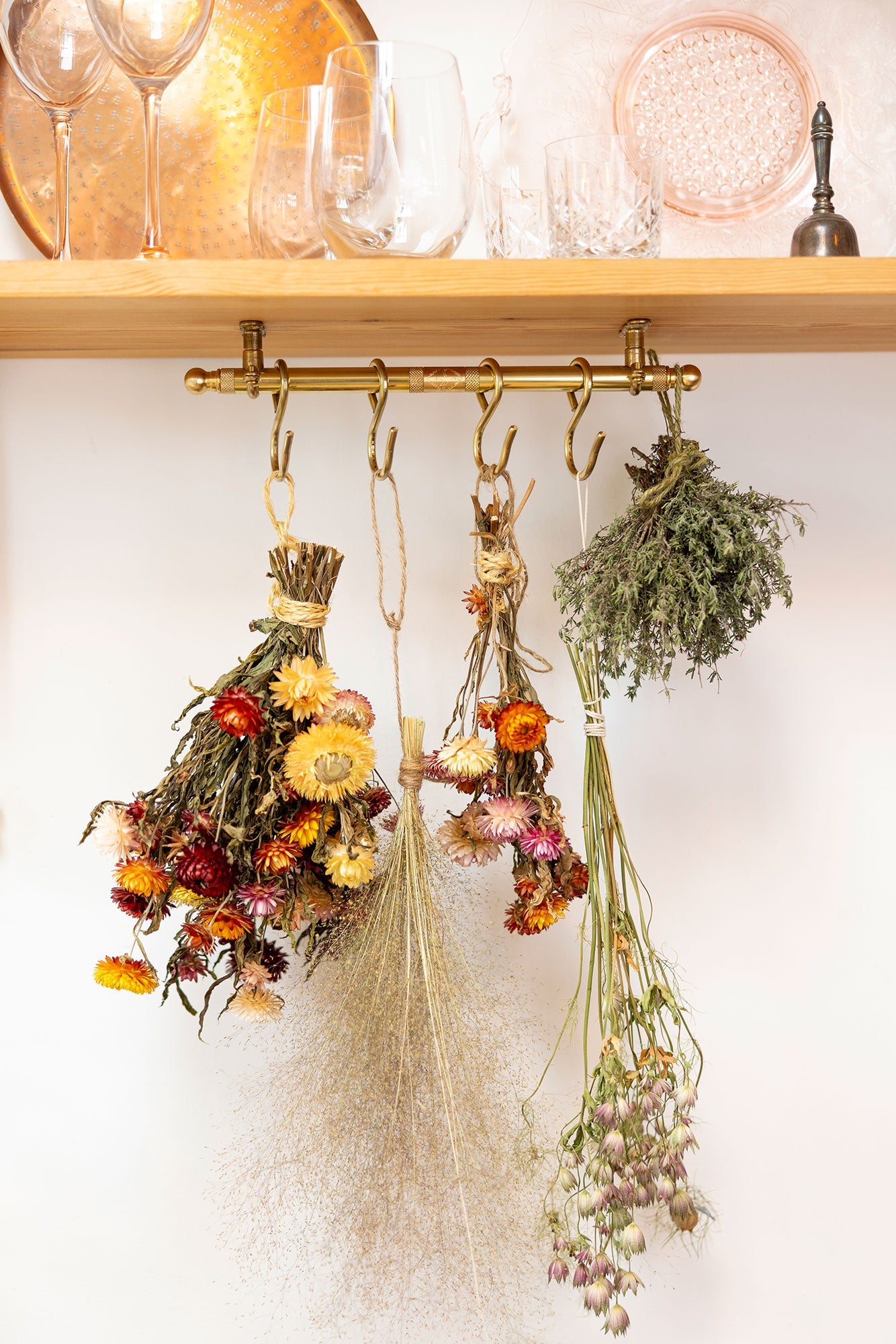 Dried flowers and herbs hanging on a brass hook against a white wall.