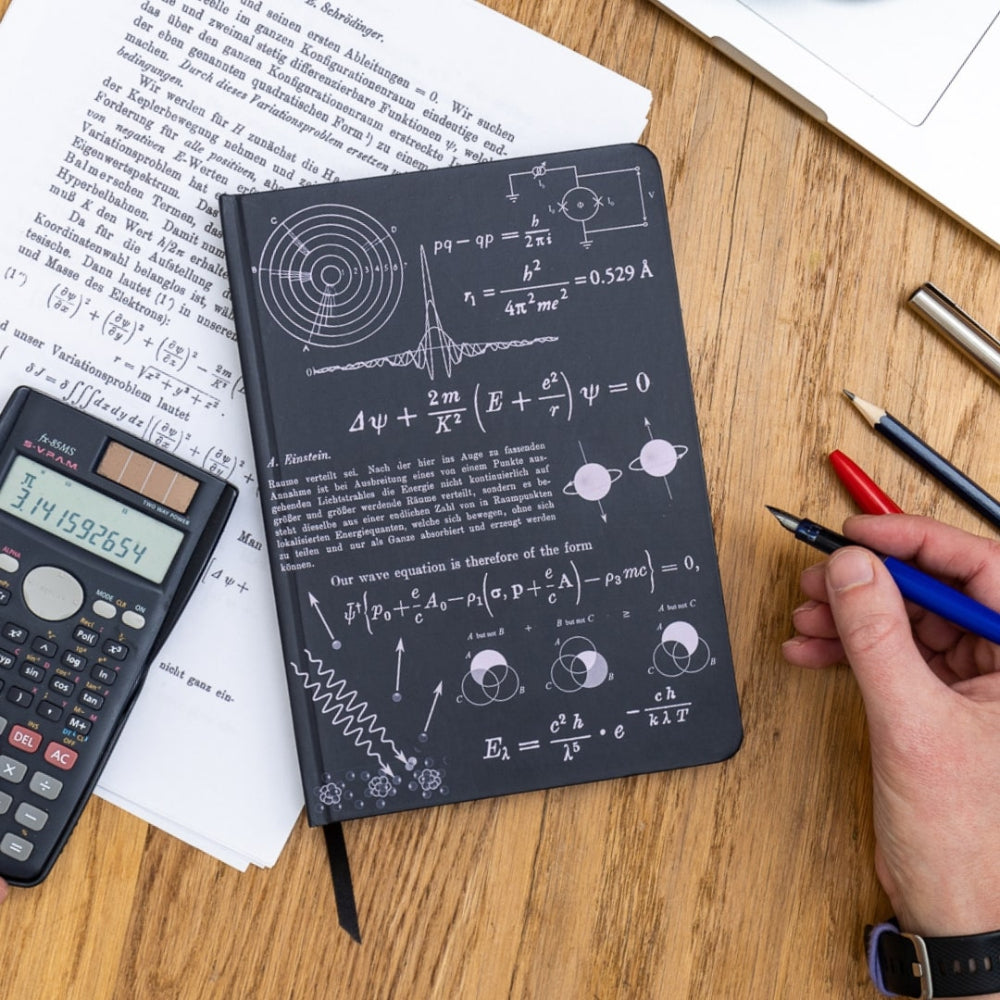 A5 Quantum Physics Notebook with scientific equations on a wooden table with a calculator and pens.