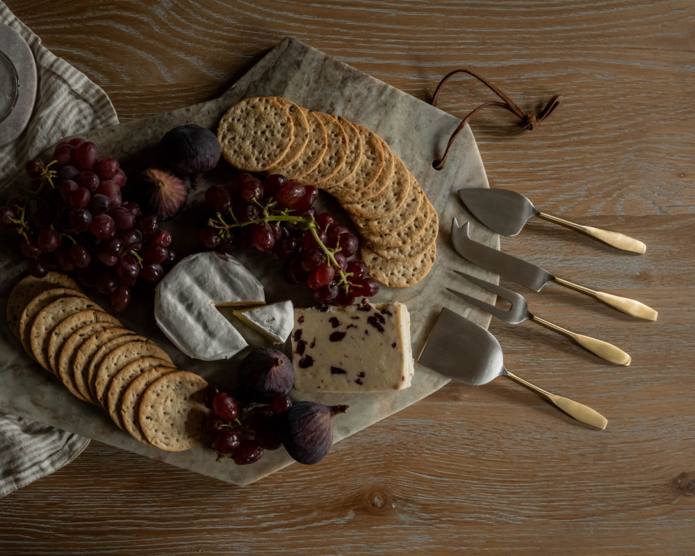 Platter of assorted cheeses, crackers, and fruits with cheese knives on a wooden surface.