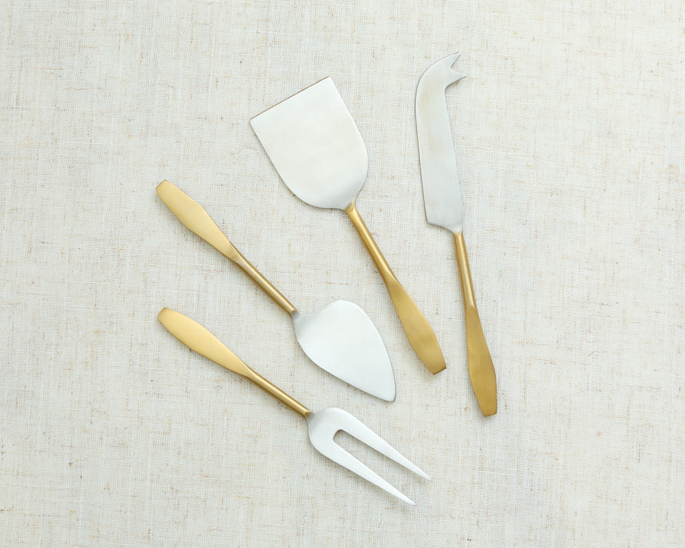 Set of gold-handled cheese tools on a textured beige surface