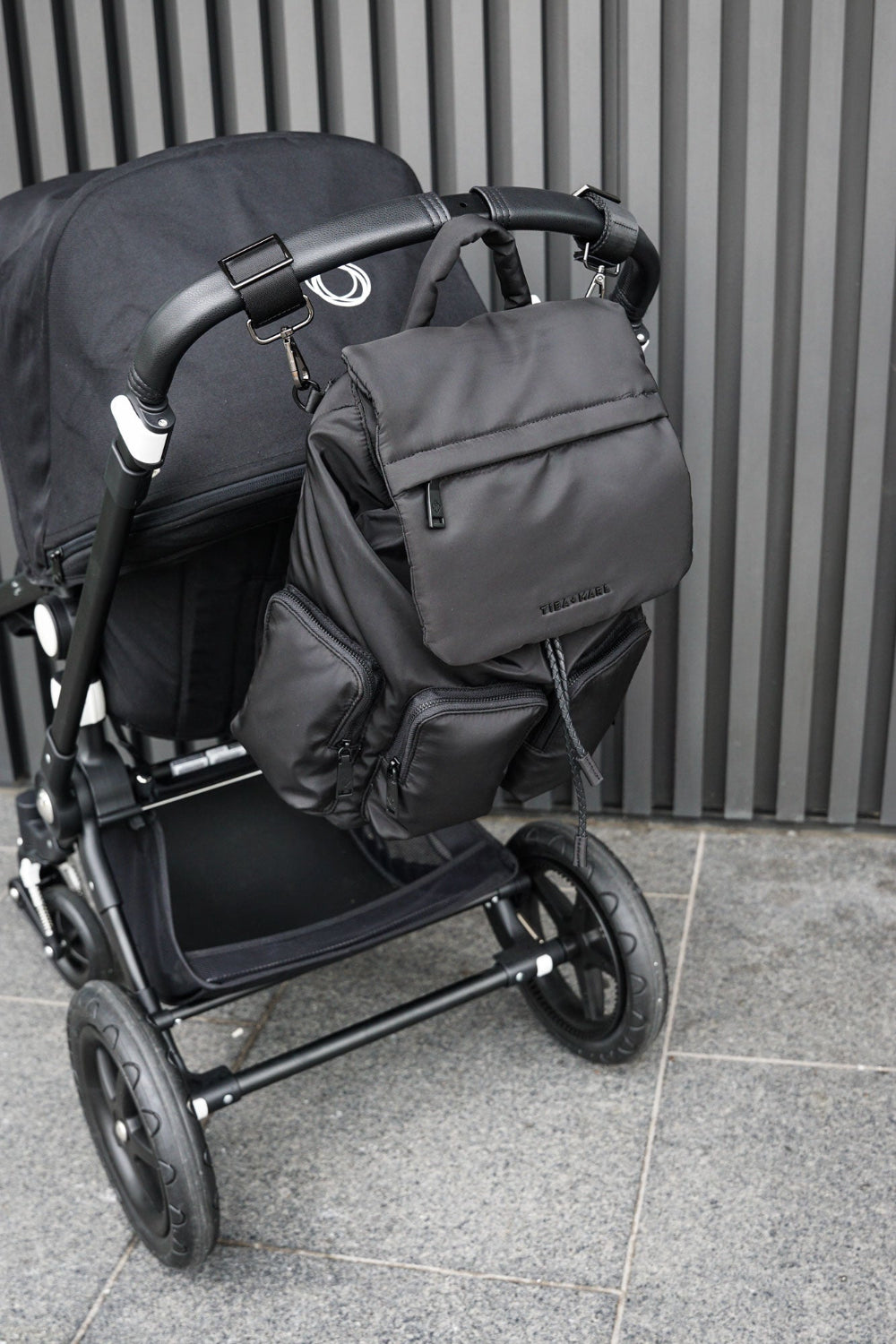 Black stroller with a matching backpack against a grey wall.