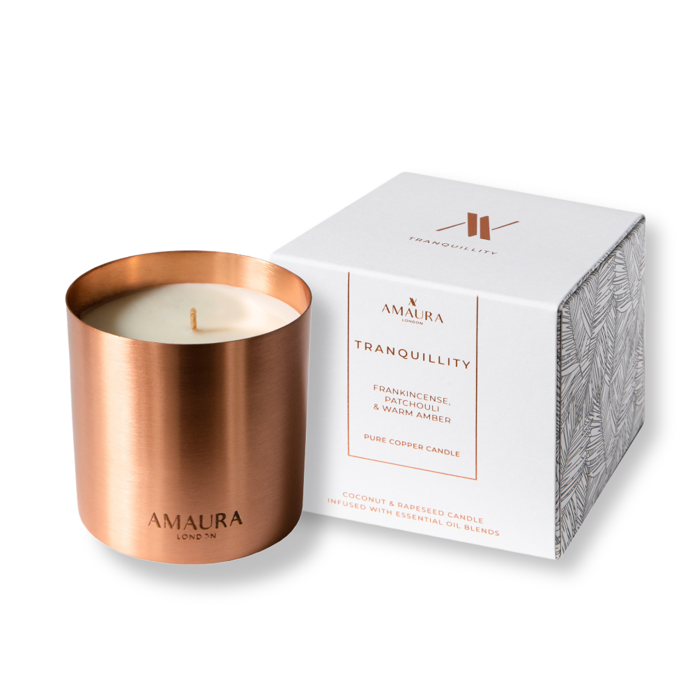 Copper candle with white candle inside and packaging labeled 'Amaura' on a white background