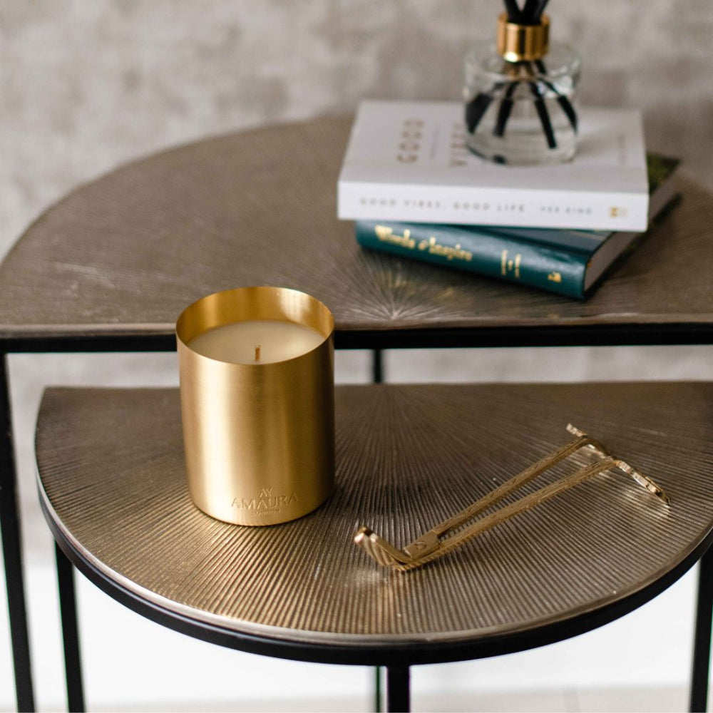 Gold candle in a textured container on a round wooden table with books and candle wick trimmer in the background.