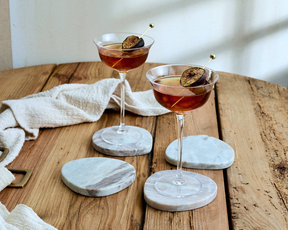 Two cocktails with figs on a wooden table with marble coasters