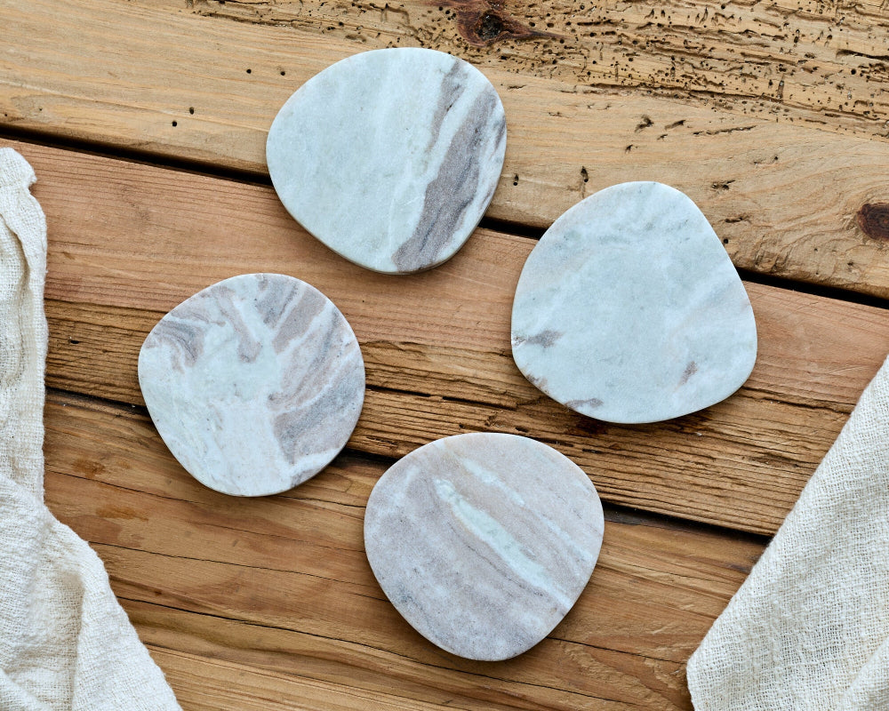 Four marble-patterned coasters on a wooden surface with a beige cloth.