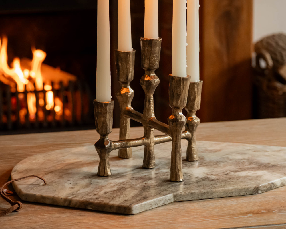 Bronze candle holder with four candles on a marble coaster in front of a fireplace.
