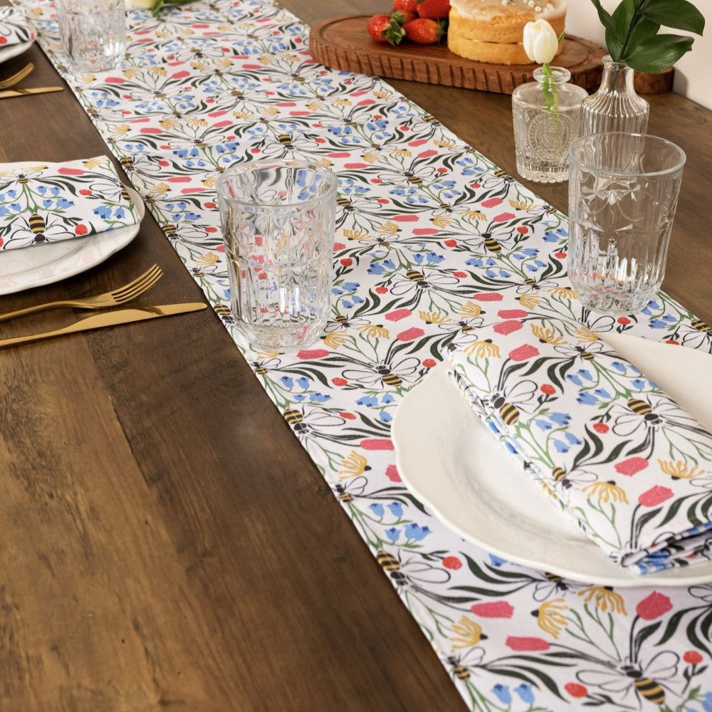 Dining table set with a floral table runner, plates, glasses, and cutlery on a wooden table.