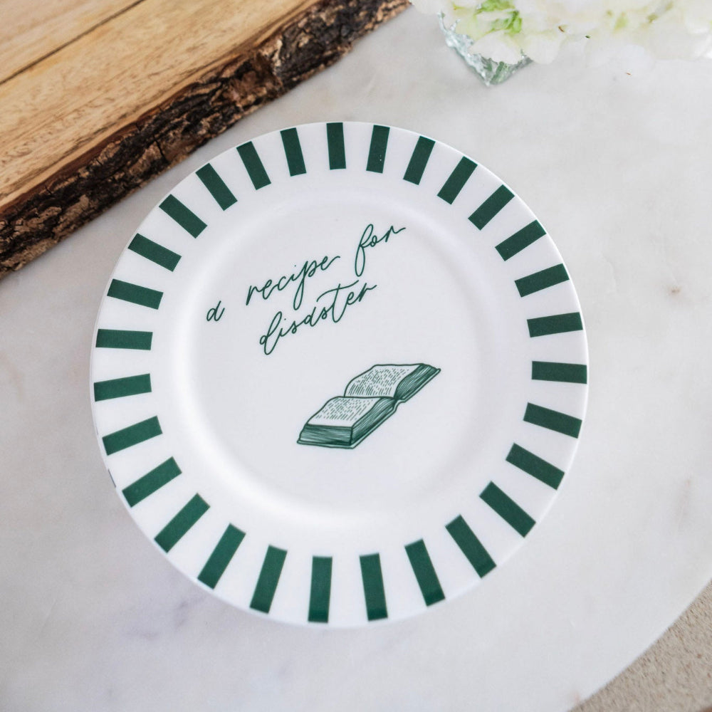 White plate with green stripes and text 'a recipe for disaster' on a light surface