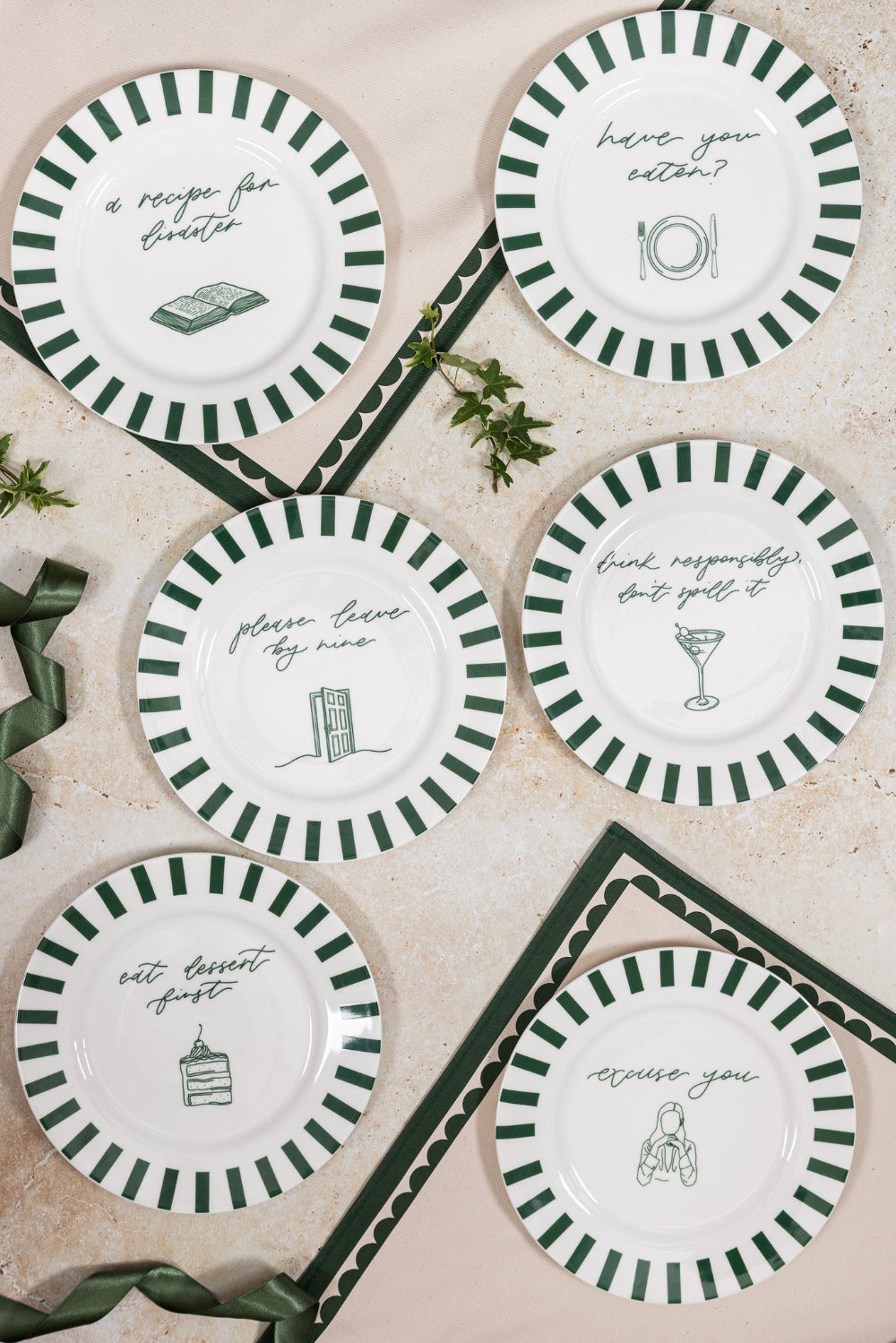Set of decorative plates with green and white stripes and humorous sayings on a textured surface.