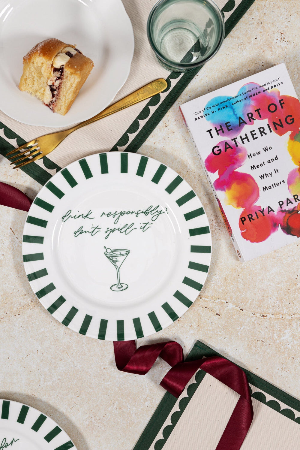 Table setting with plates, a glass, a roll of bread, and a book titled 'The Art of Gathering' on a beige surface.