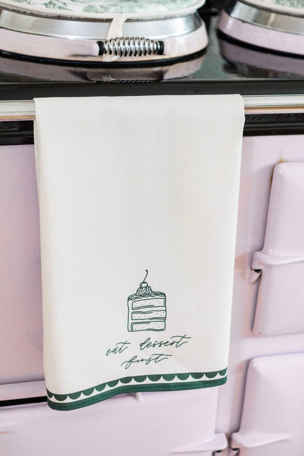 White tea towel with green cake illustration and text hanging on a stove.