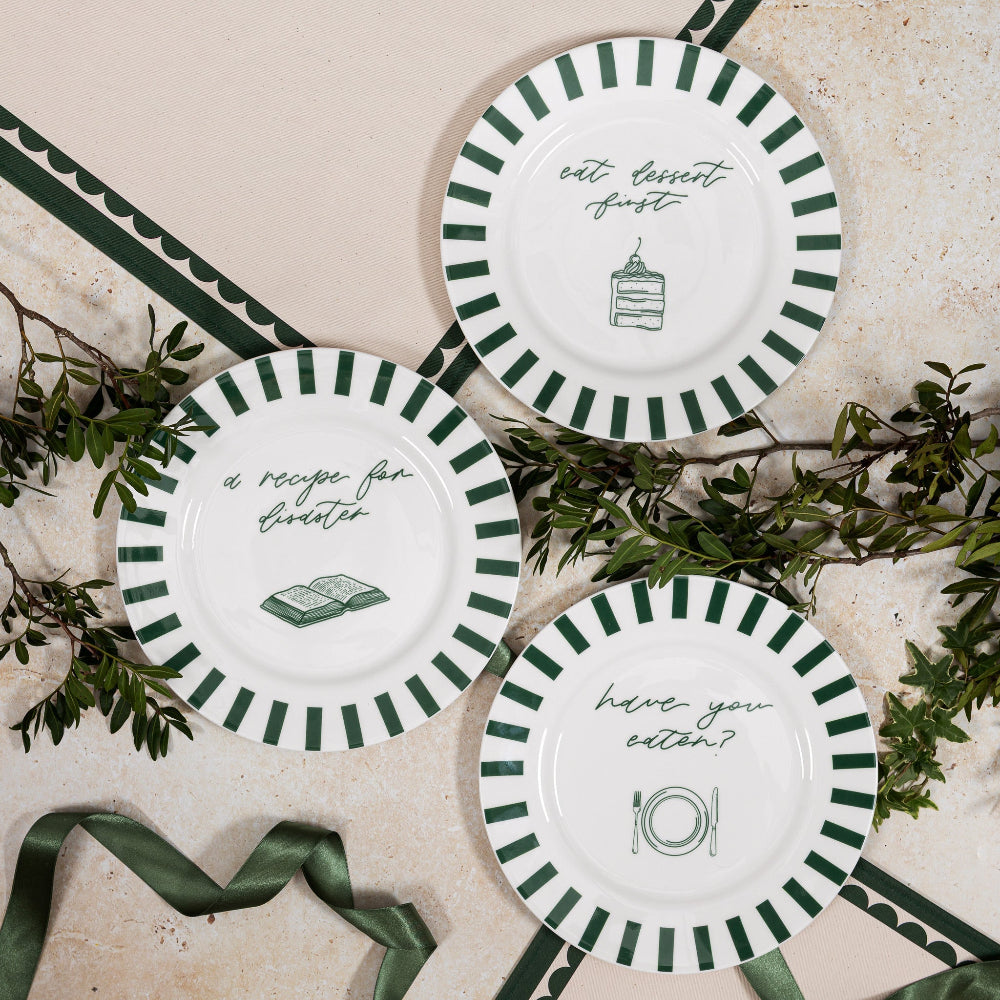 Three decorative plates with green and white stripes and text on a stone surface with greenery.