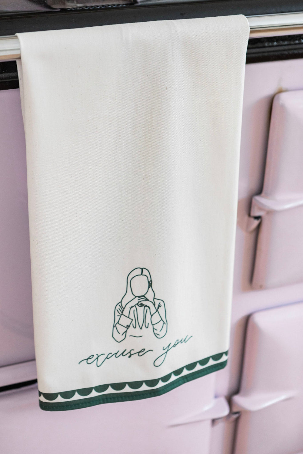 Tea towel with green border and printed design hanging on a stove.