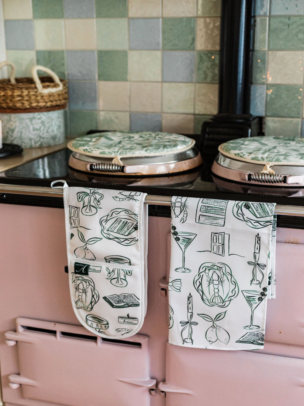 Pink kitchen stove with green tiled wall and patterned towels.