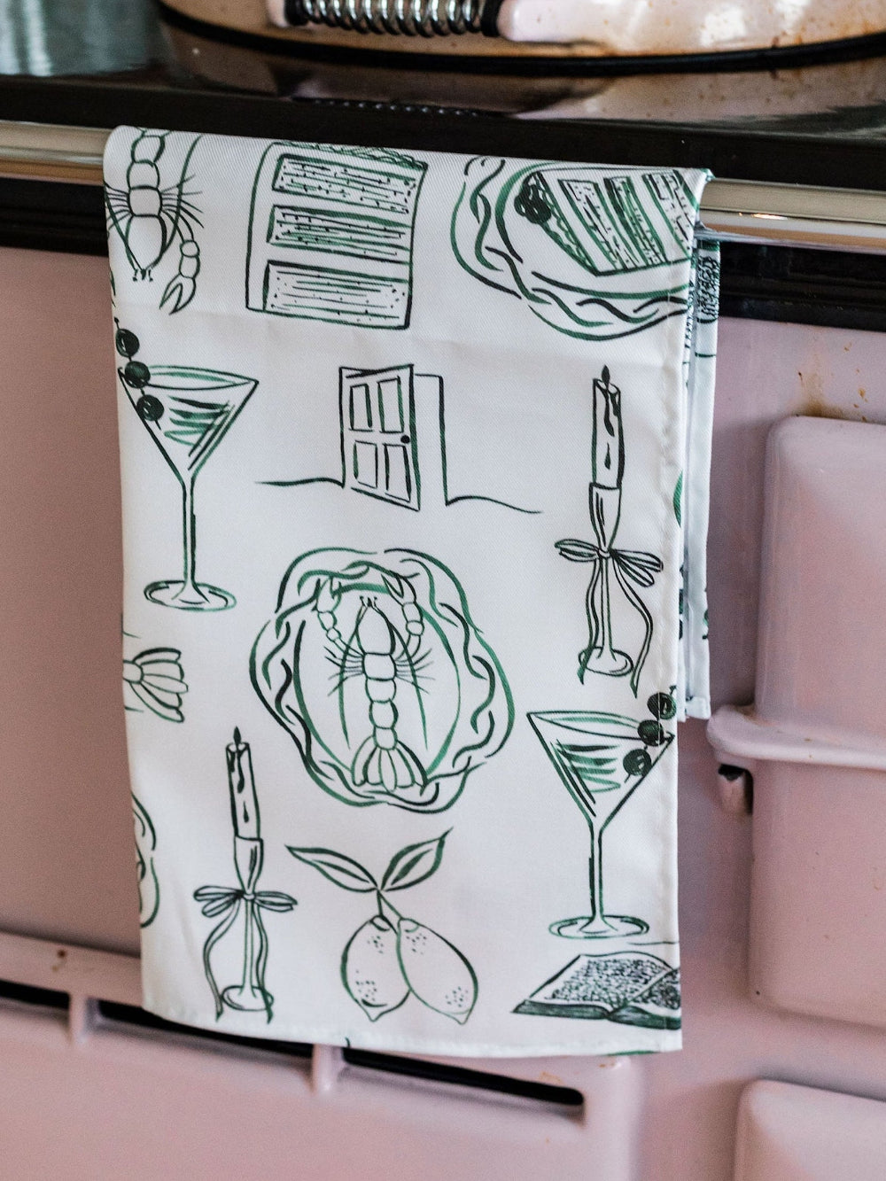 Kitchen towel with green illustrations hanging on a stove handle