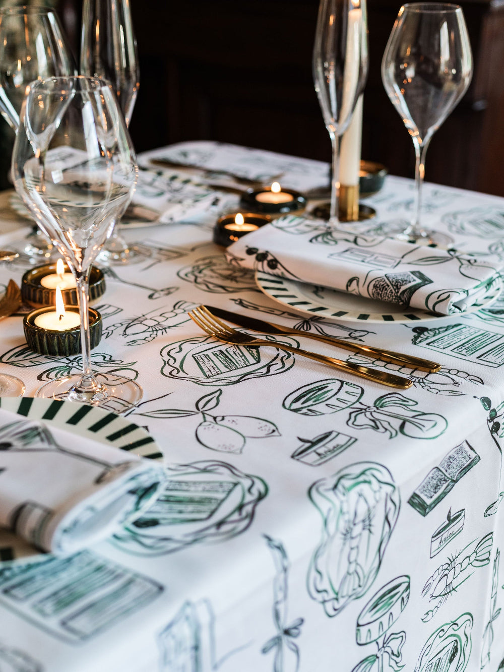 Table setting with wine glasses, candles, and a decorative tablecloth featuring illustrations.