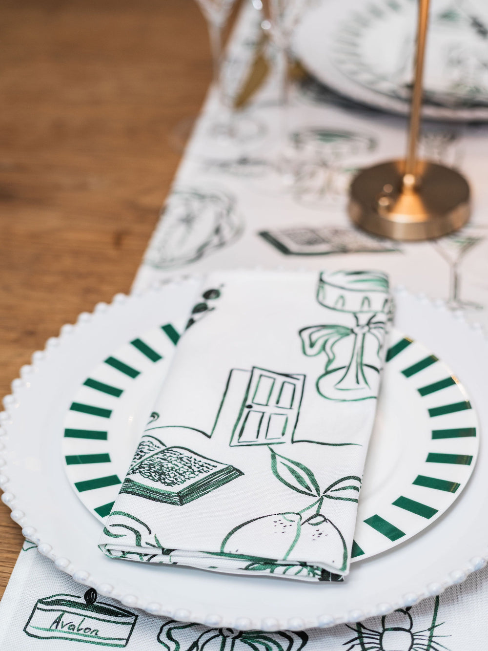 Table setting with decorative plates and napkins featuring green and black patterns on a wooden table.