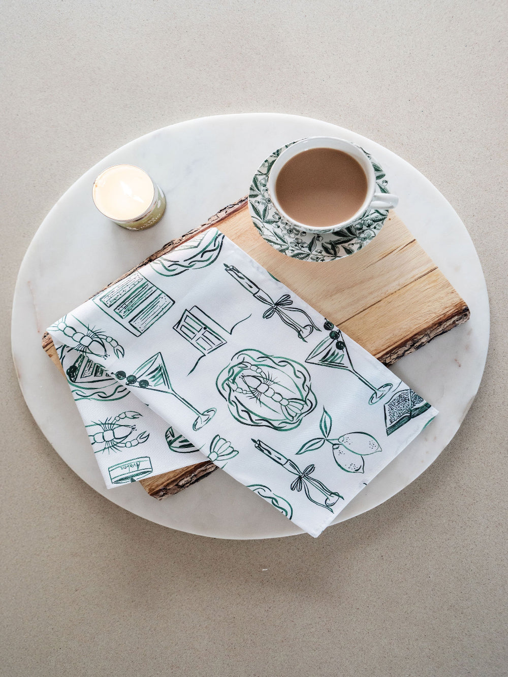 Tea cup, wooden block, and tea towel with illustrations on a beige background