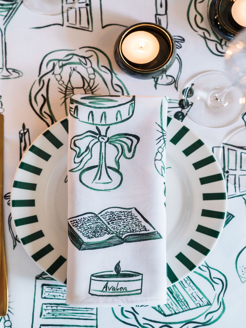Table setting with a decorative towel featuring illustrations of books and candles on a white tablecloth.