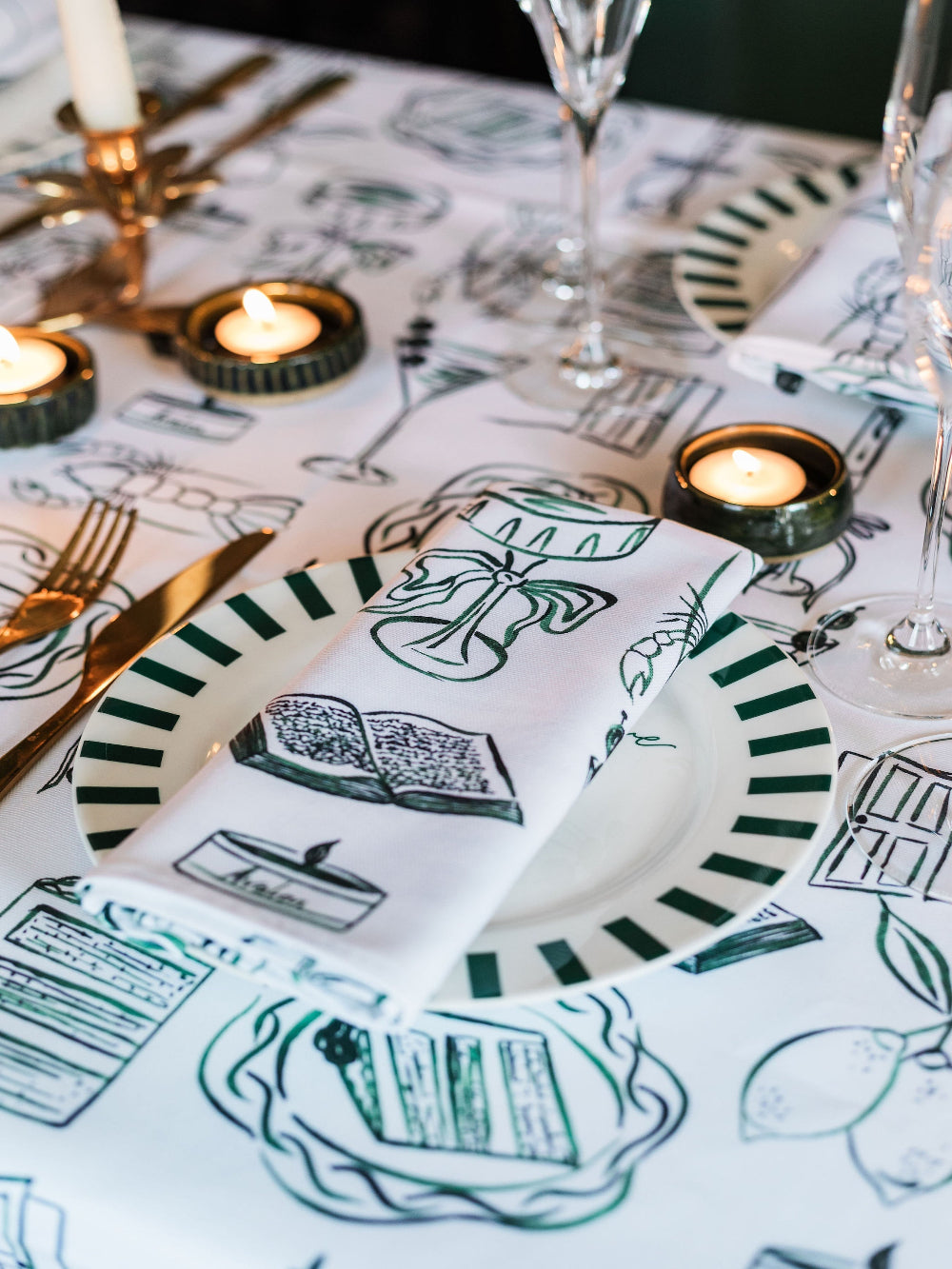 Table setting with decorative plates, napkins, and candles on a tablecloth with illustrations.