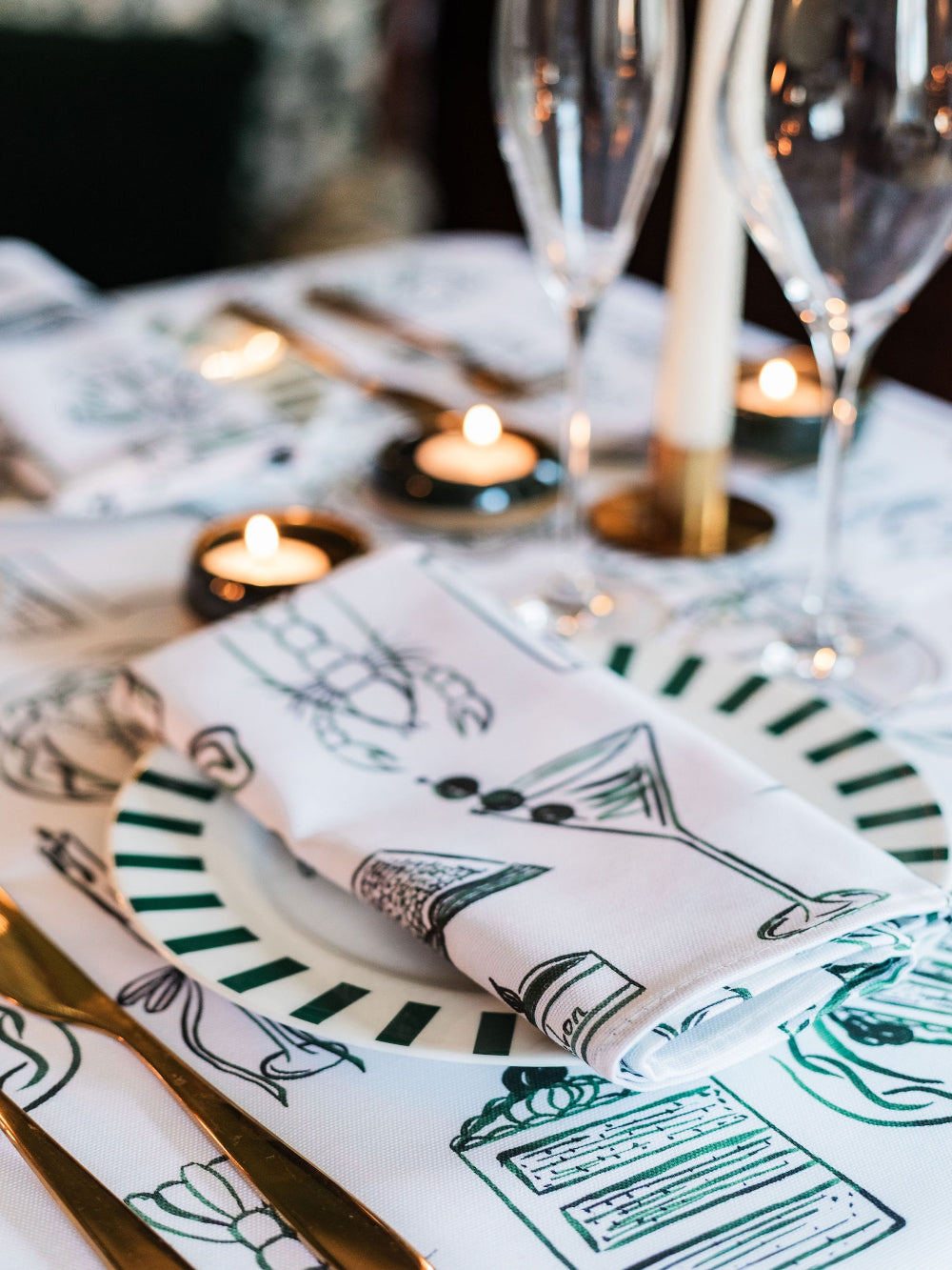 Table setting with patterned napkins and plates, candles, and glasses.