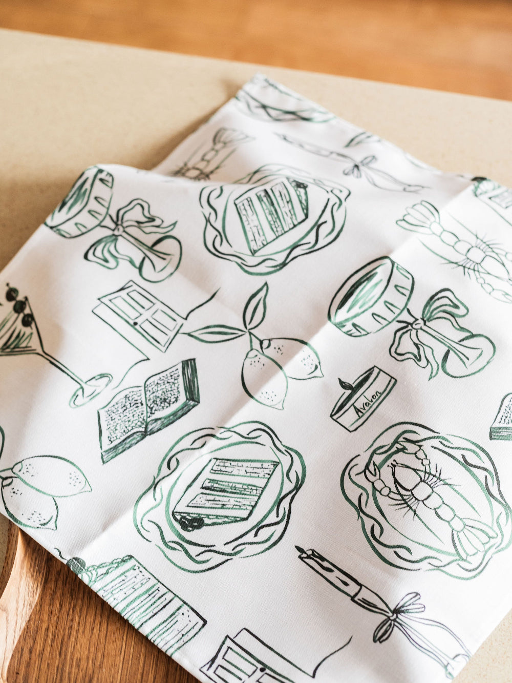 White napkin with green illustrations of books and quills on a wooden surface