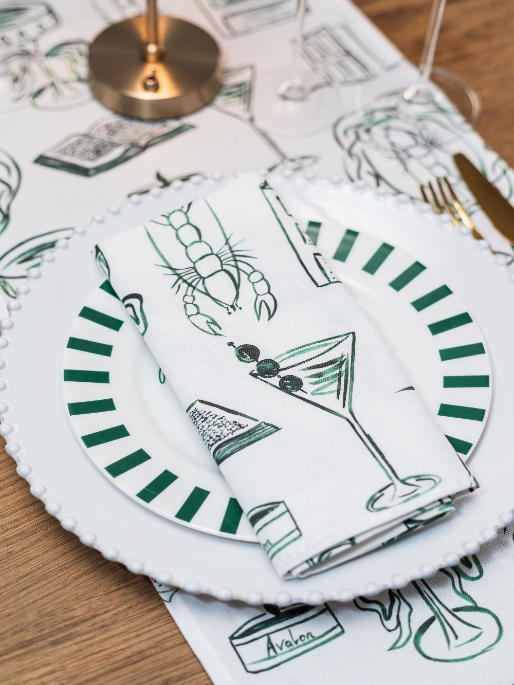 Table setting with white plates, green striped napkins, and a cocktail-themed placemat.