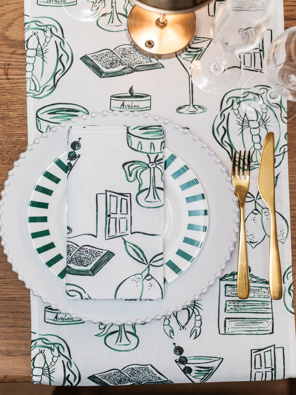 Table setting with white plates, gold cutlery, and a decorative placemat with green and black patterns.