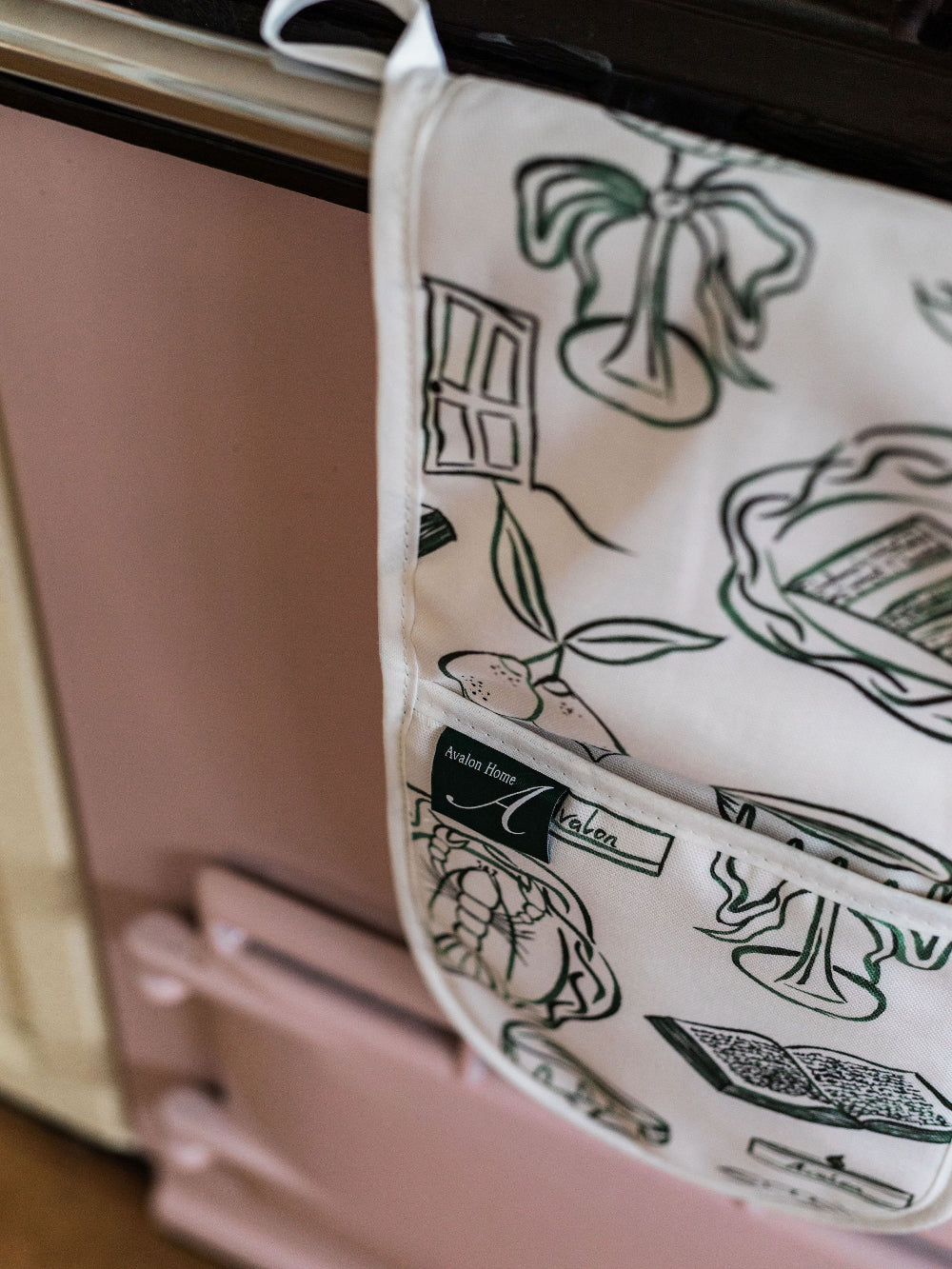 Oven Mitts with green illustrations hanging on a pink oven.