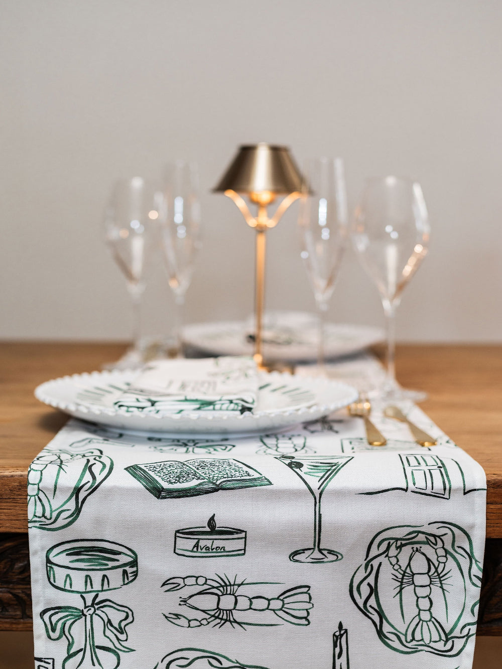 Table setting with a decorative table runner featuring green illustrations on a white background.