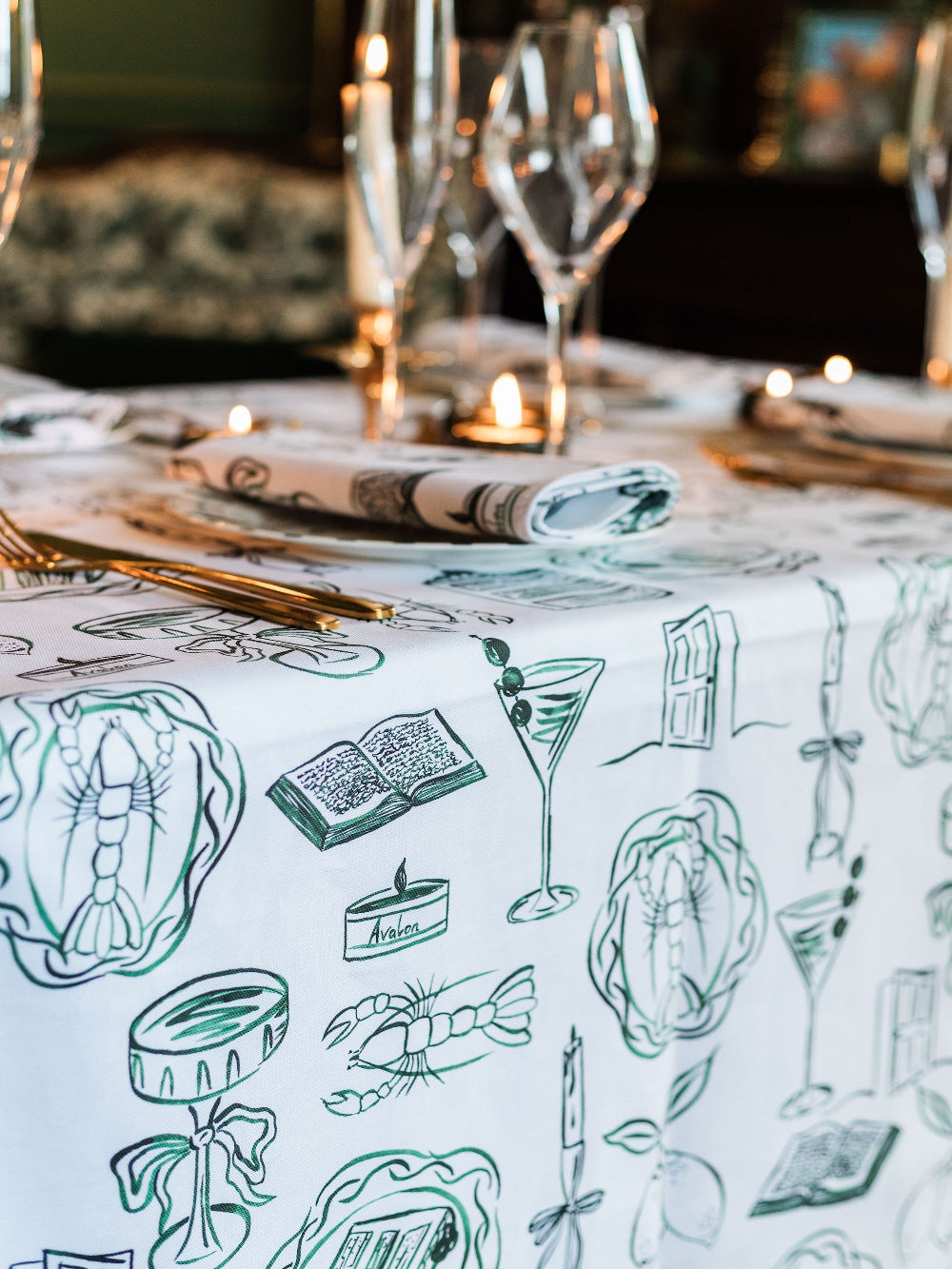 Table setting with a decorative tablecloth featuring illustrations of drinks and food items.